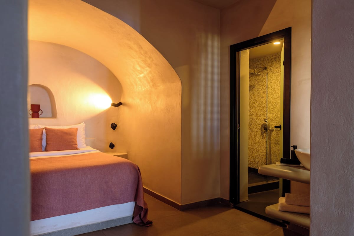 A bedroom with a curved wall, a bed, a nightstand, and a bathroom visible through an archway.