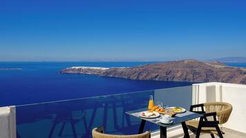 Una mesa con alimentos para el desayuno y sillas en un balcón con vistas al mar y a los acantilados.