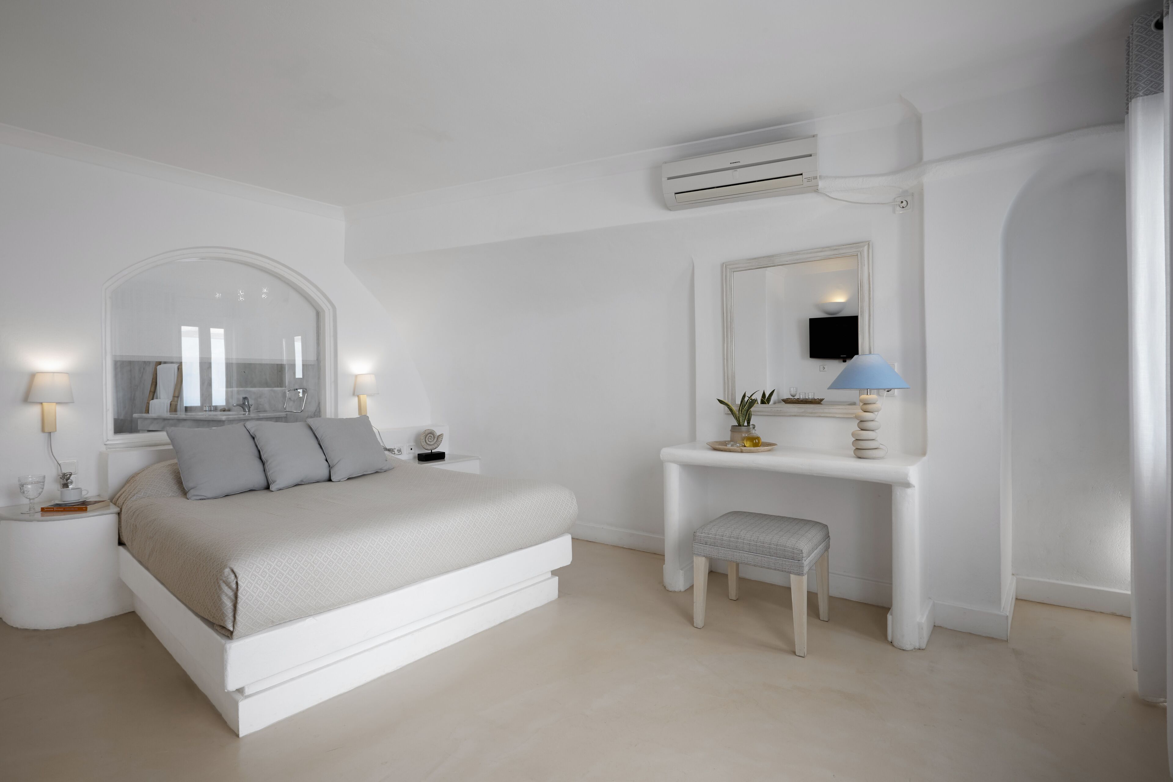A minimalist bedroom with a bed, bedside tables, a vanity with a mirror, and an air conditioning unit.