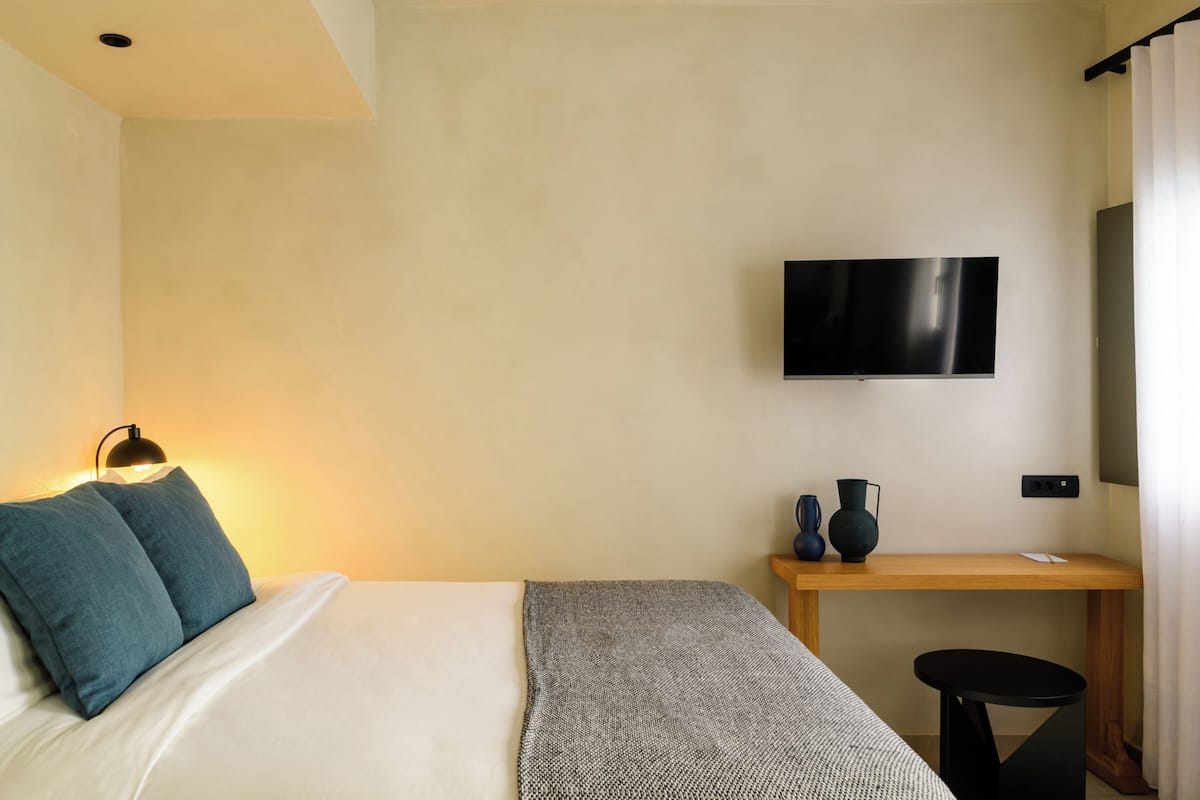 A hotel room with a bed, a desk, a television, and a small table.