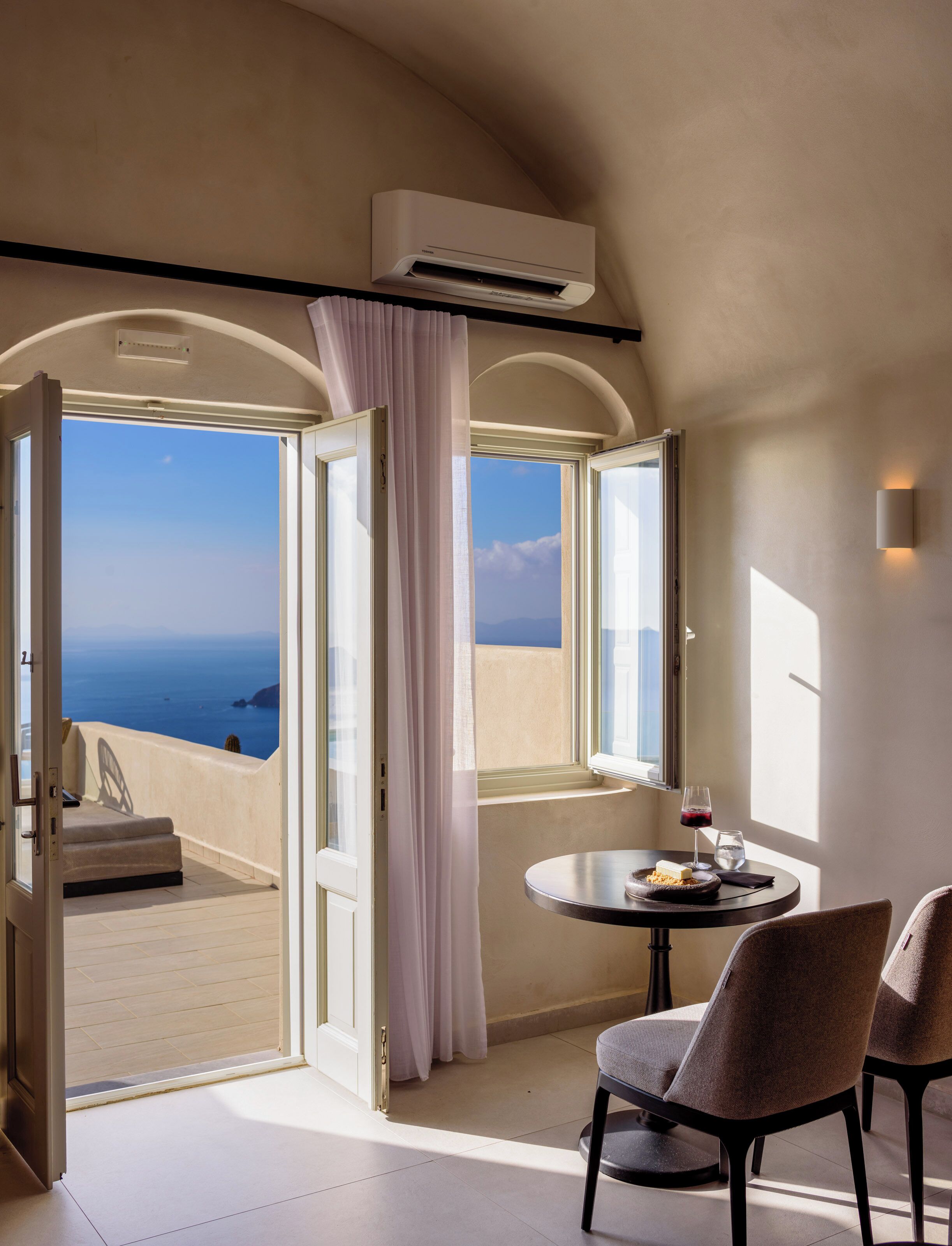 Una stanza con vista sul mare, un tavolo rotondo con sedie e una porta aperta che dà su un balcone.