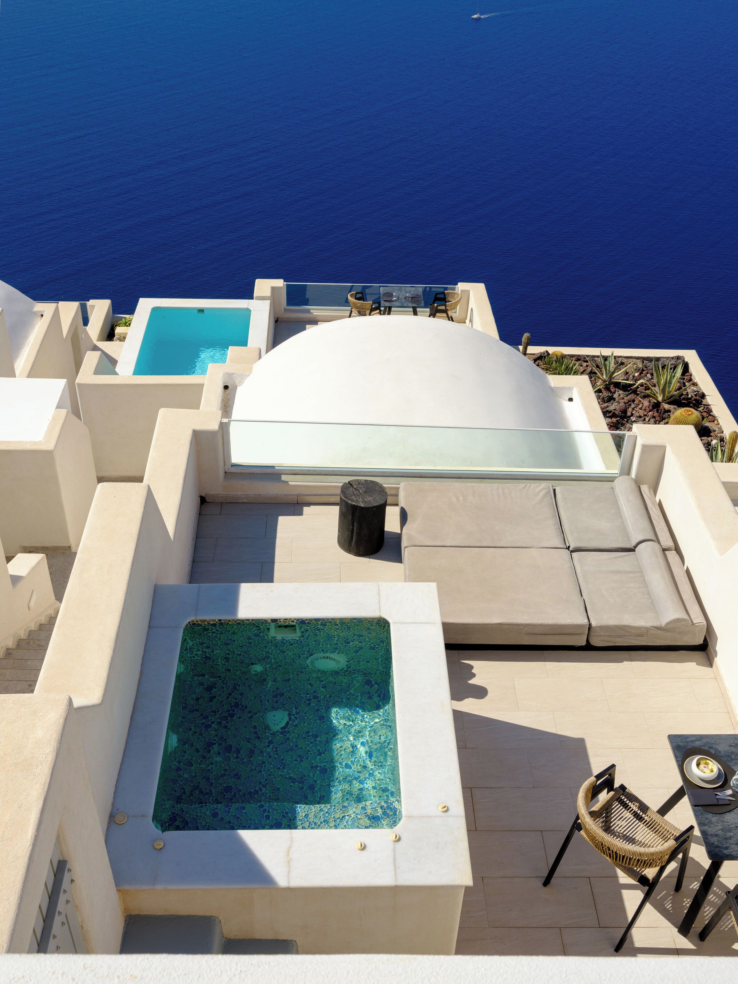 A rooftop pool area with a glass-enclosed hot tub, a seating area with cushions, and a view of the ocean.