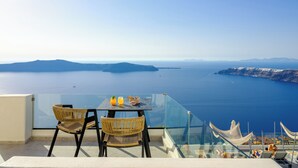 Une table en verre, entourée de chaises en osier, sur un balcon donnant sur la mer.