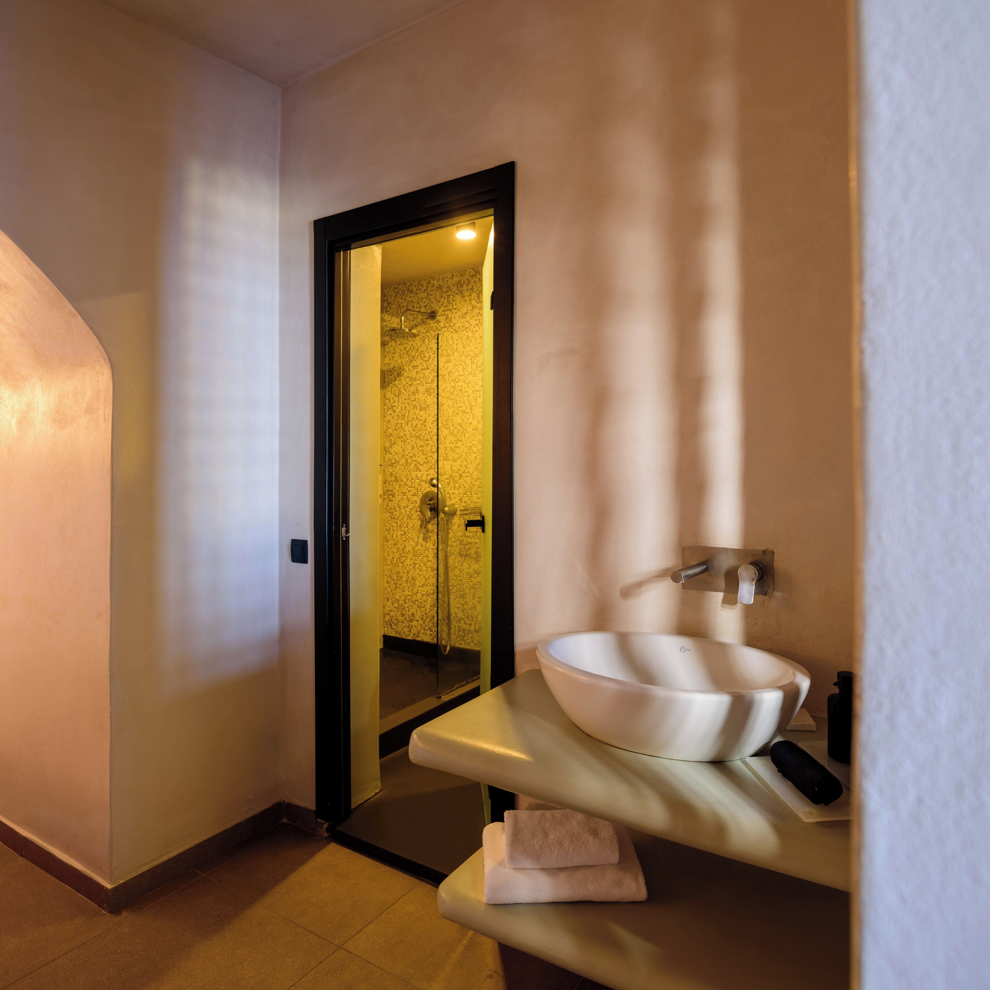 A modern bathroom with a large white sink, a glass shower enclosure, and a towel on the counter.