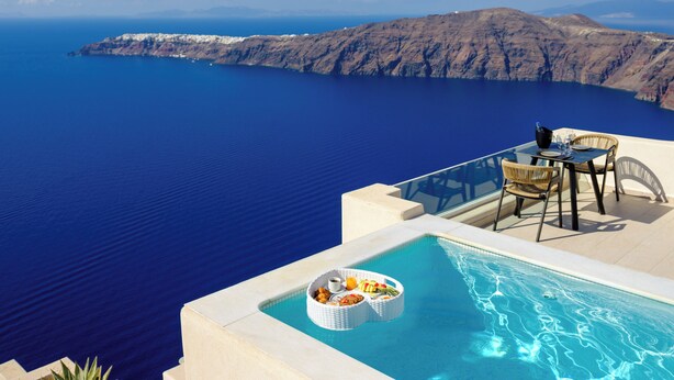 Une piscine avec une table et des chaises, donnant sur une étendue d’eau et un paysage montagneux.