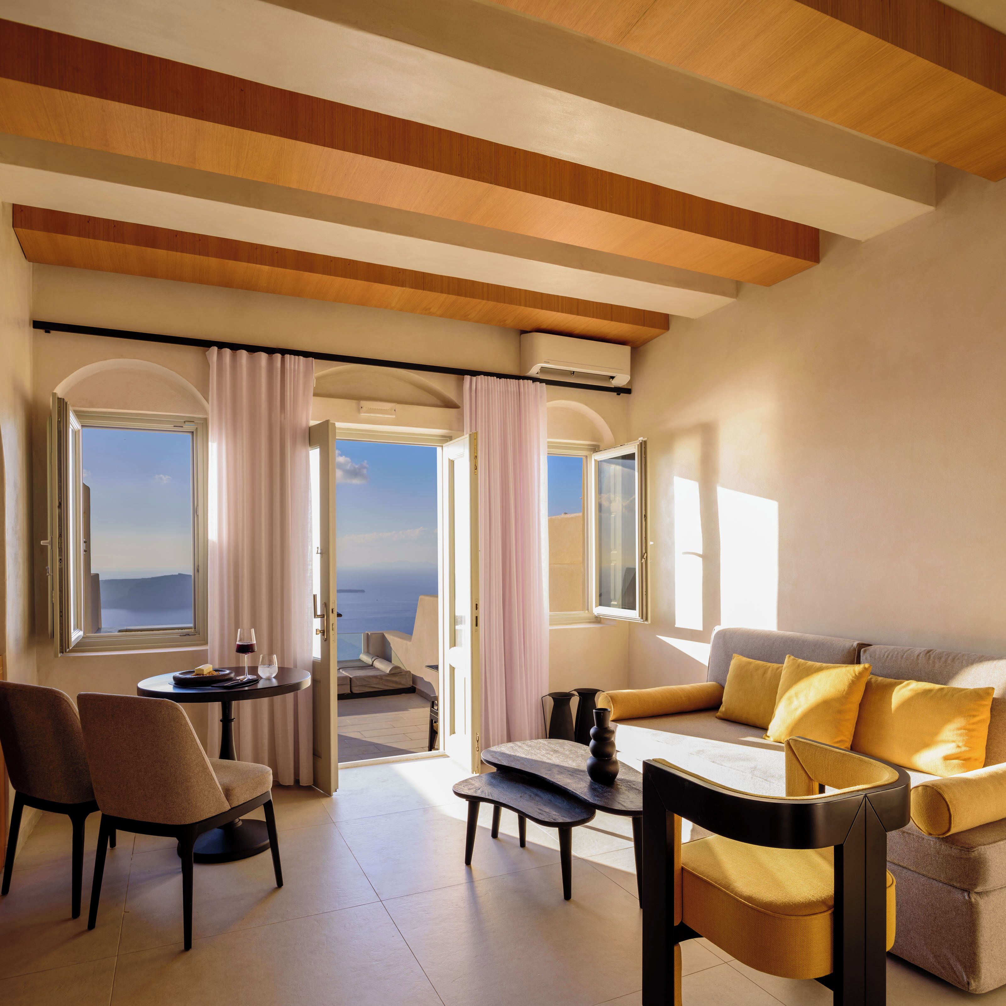 Quarto de hotel moderno com varanda, sofá, mesa de jantar e cadeiras.