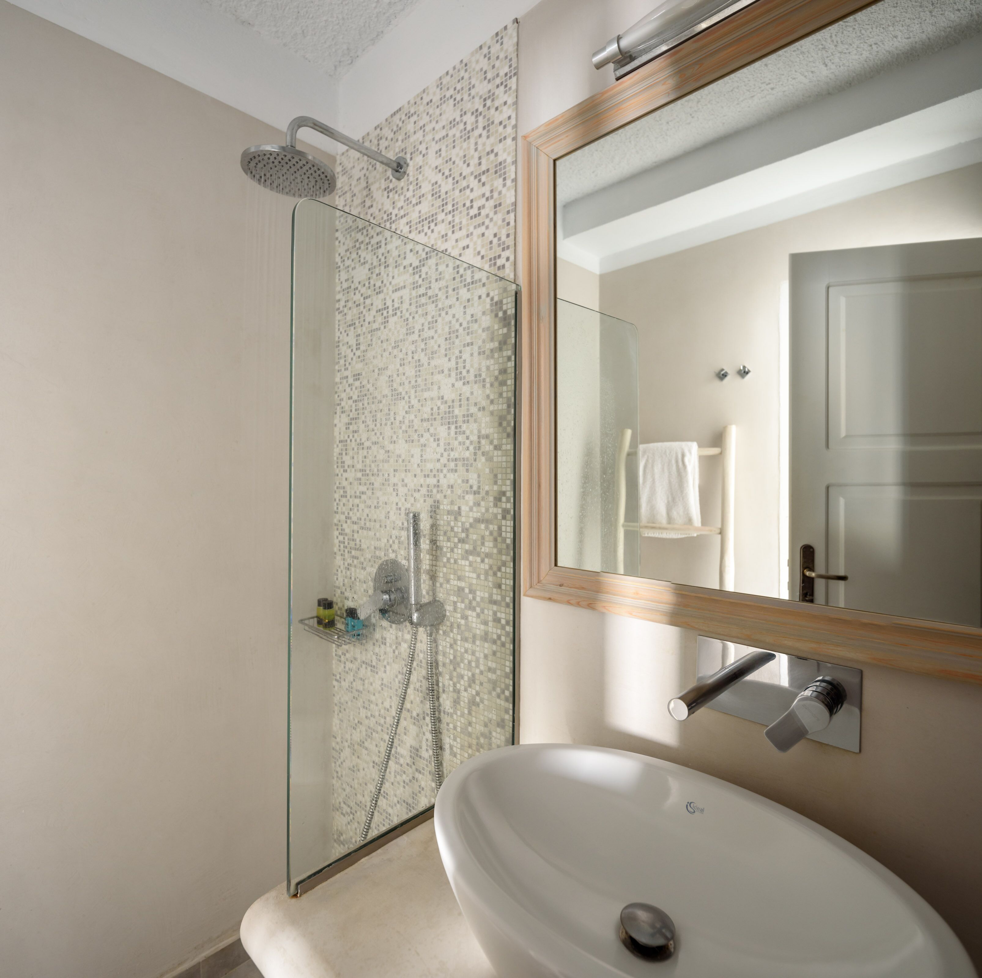 A modern bathroom with a glass shower enclosure, a white sink, and a large mirror with a wooden frame.