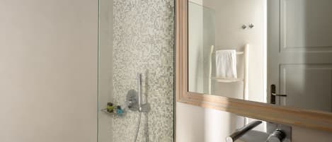 A modern bathroom with a glass shower enclosure, a white sink, and a large mirror with a wooden frame.