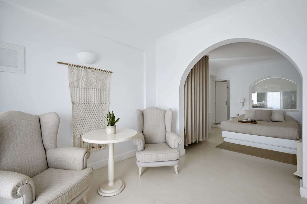 A minimalist bedroom with a large bed, two armchairs, a small table, and a decorative macrame curtain.