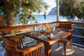 A wooden table with breakfast items and a glass of orange juice on a balcony overlooking the sea. - Alesahne Beach (Santorini)