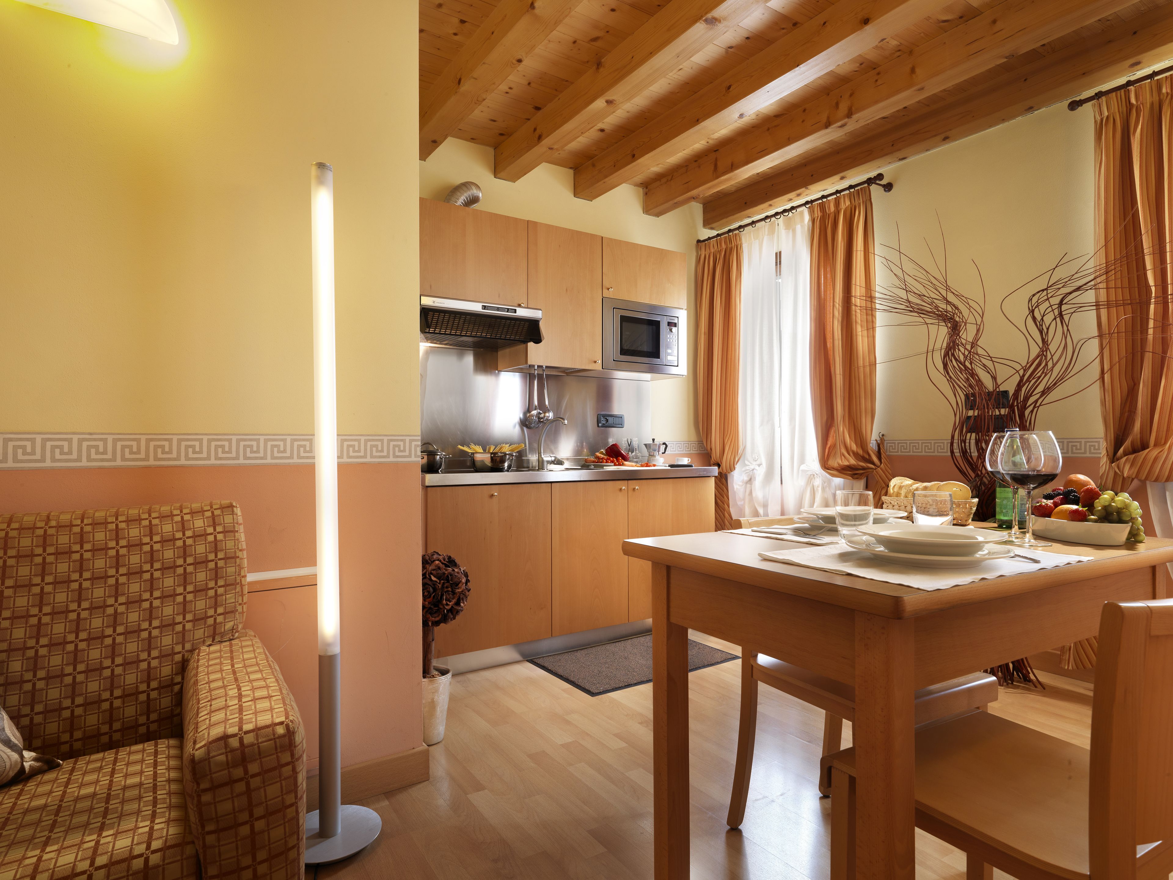 A cozy dining area with a wooden table set for two, a sofa, and a kitchen in the background.