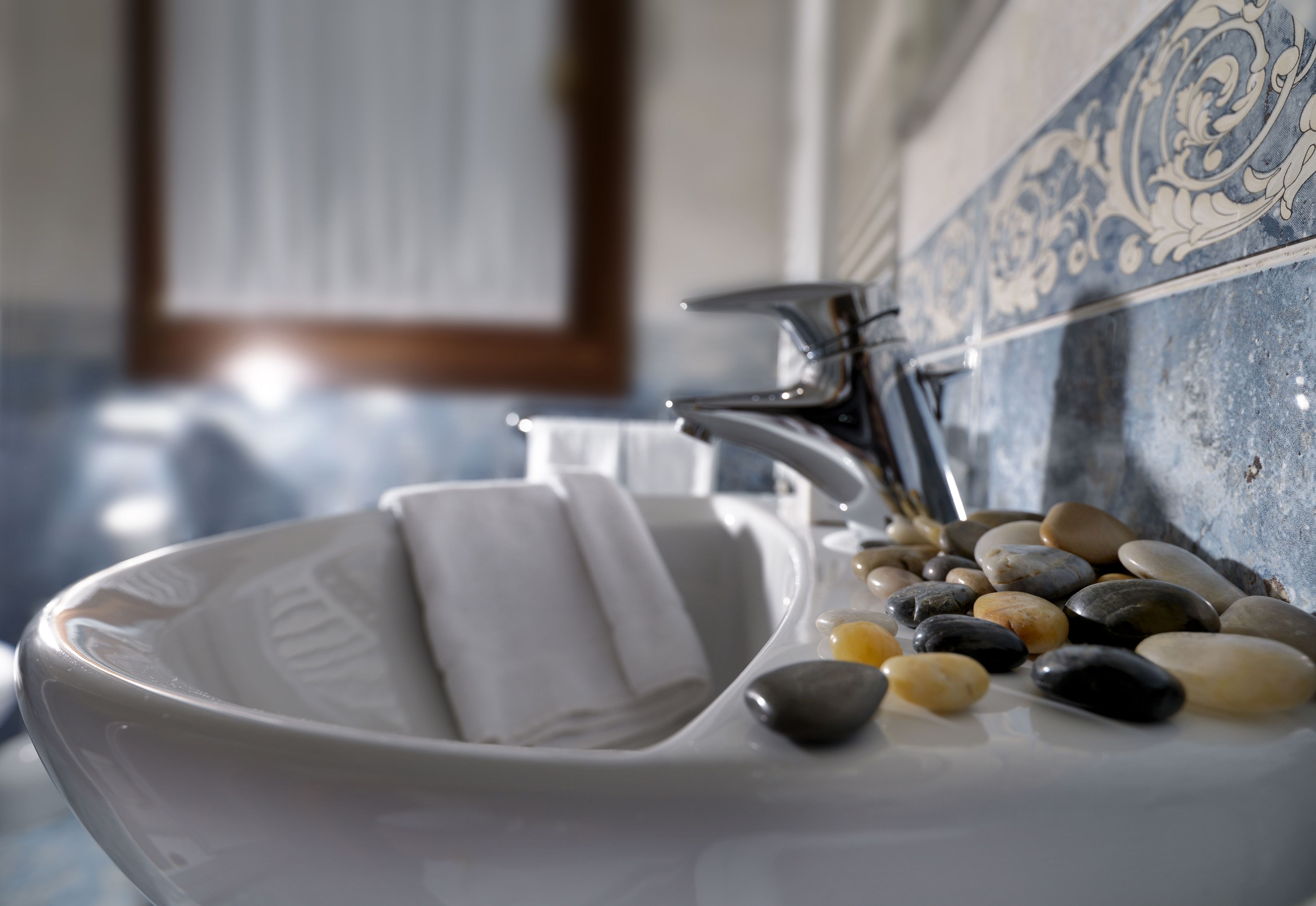 A white ceramic sink with a faucet, surrounded by smooth stones and a decorative tile backsplash.
