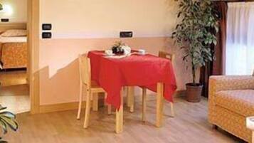 Ein gemütlicher Raum mit Esstisch, gedeckter Tischdecke rot, einer Couch und einem Topf mit Pflanze.
