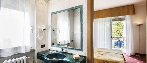 A bathroom with a sink, mirror, and toilet. There is a window with curtains and a radiator.