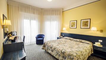 A hotel room with a bed, a desk with a telephone, a chair, and two framed pictures on the wall.