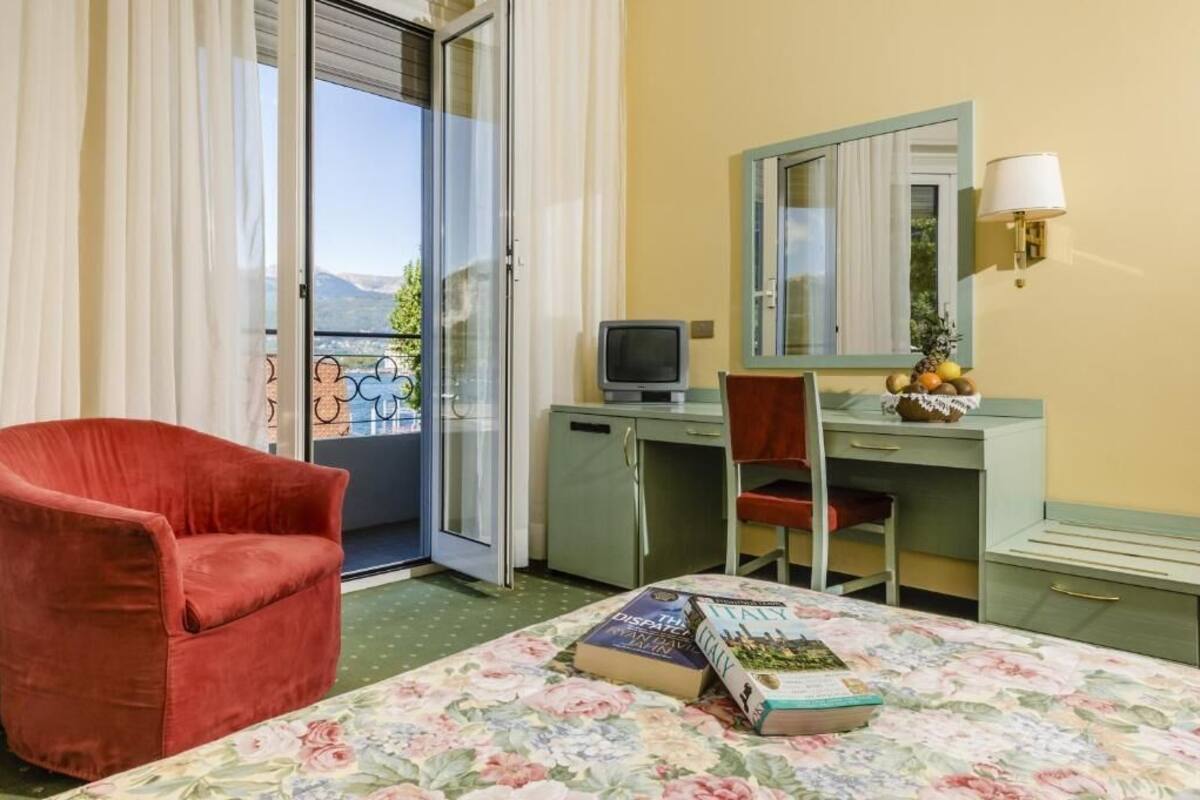 Een kamer met een bed, een bureau, een stoel, een televisie en een raam met gordijnen.