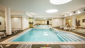 Une grande piscine intérieure dotée de nombreuses chaises longues et d’une table avec des boissons.
