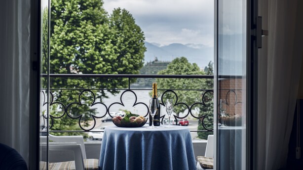 Un balcon avec une table dressée pour deux personnes, agrémentée d’une bouteille de champagne, de deux verres et d’un panier de fruits.