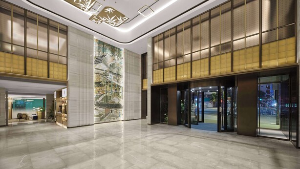 Un hall espacioso con diseño moderno, que cuenta con una gran pared cubierta de jardín vertical y un techo con luminarias geométricas.
