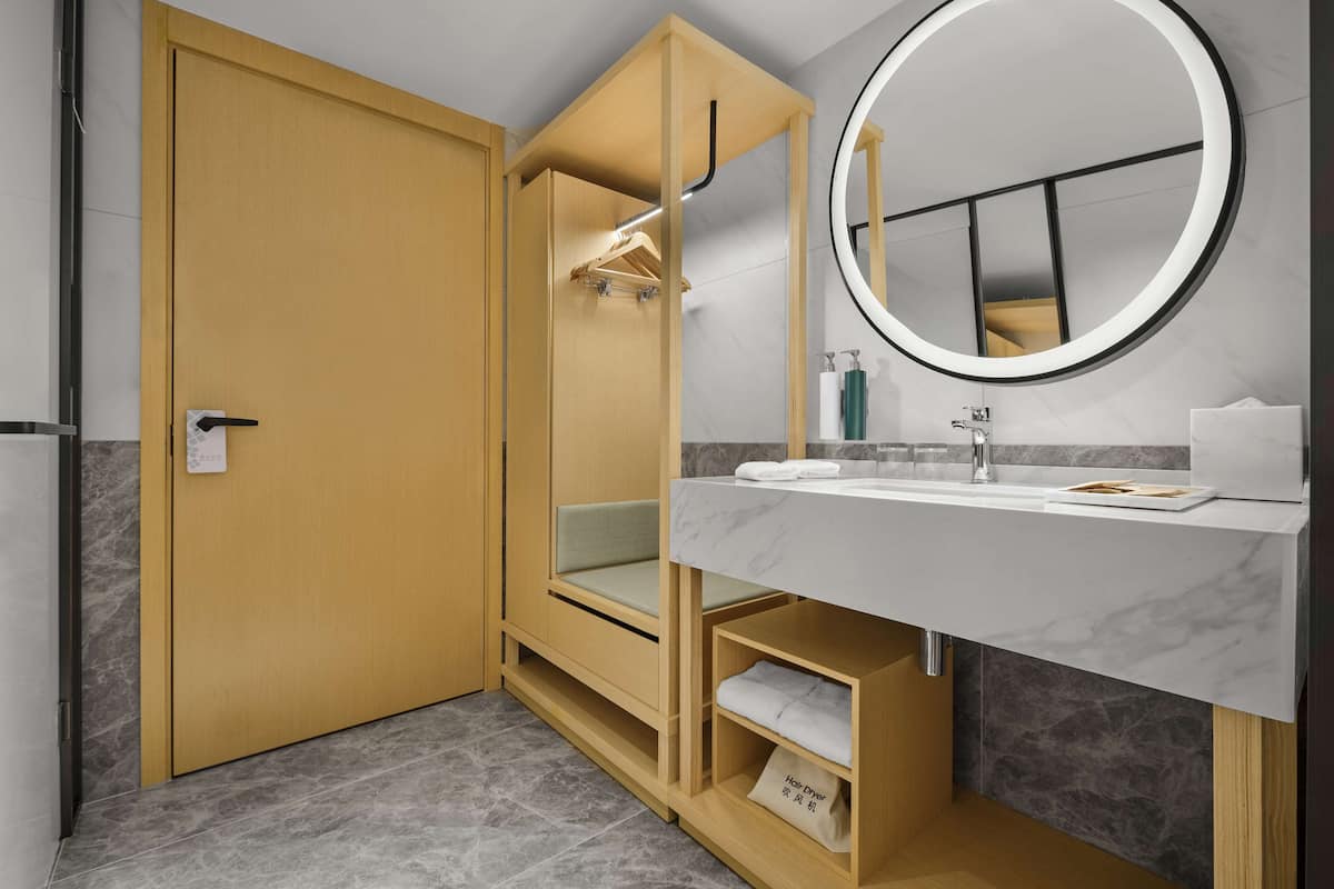 A modern bathroom with a wooden vanity, a round mirror, and a towel rack.