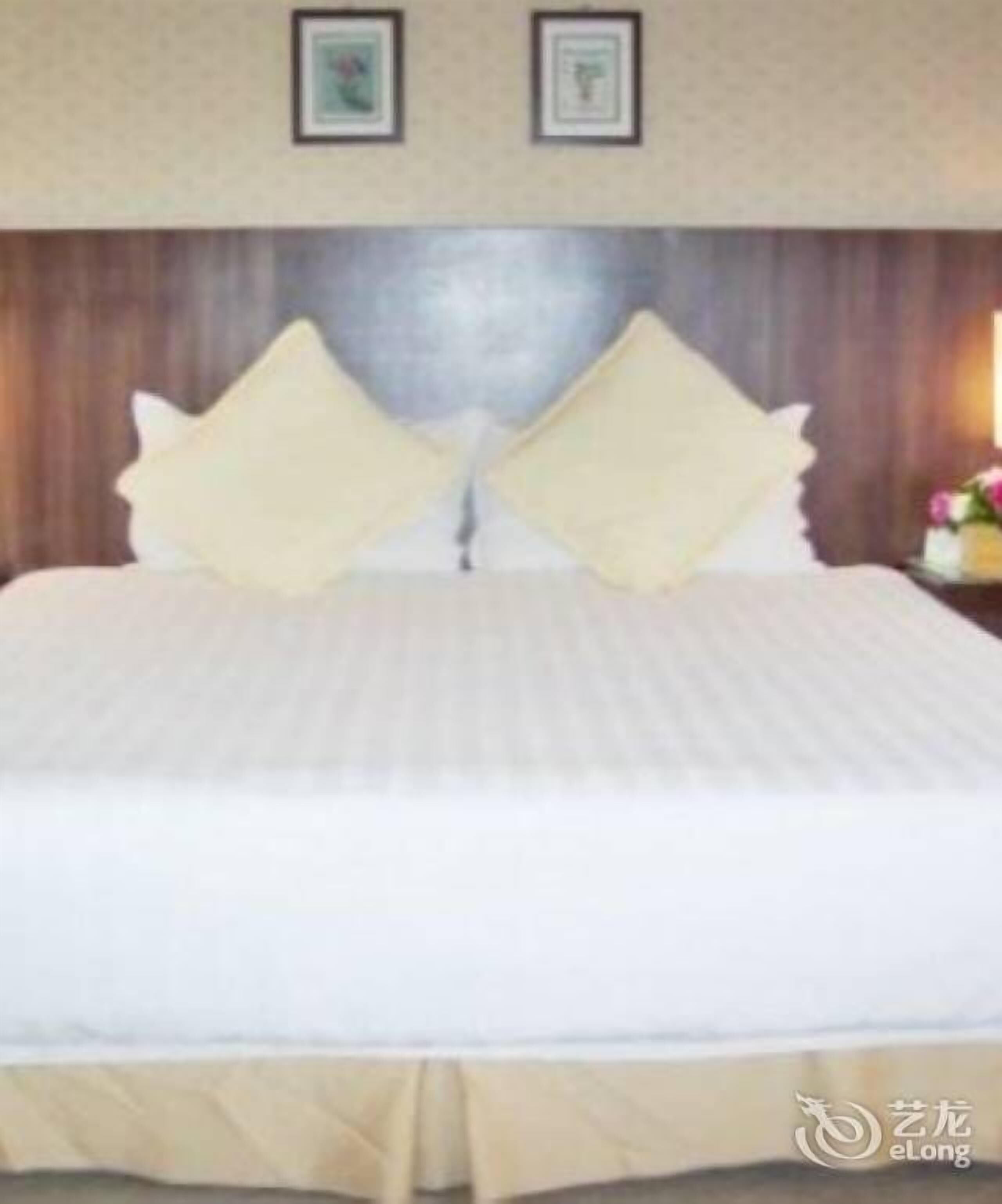 A hotel room with a large bed, wooden headboard, and two framed pictures on the wall.