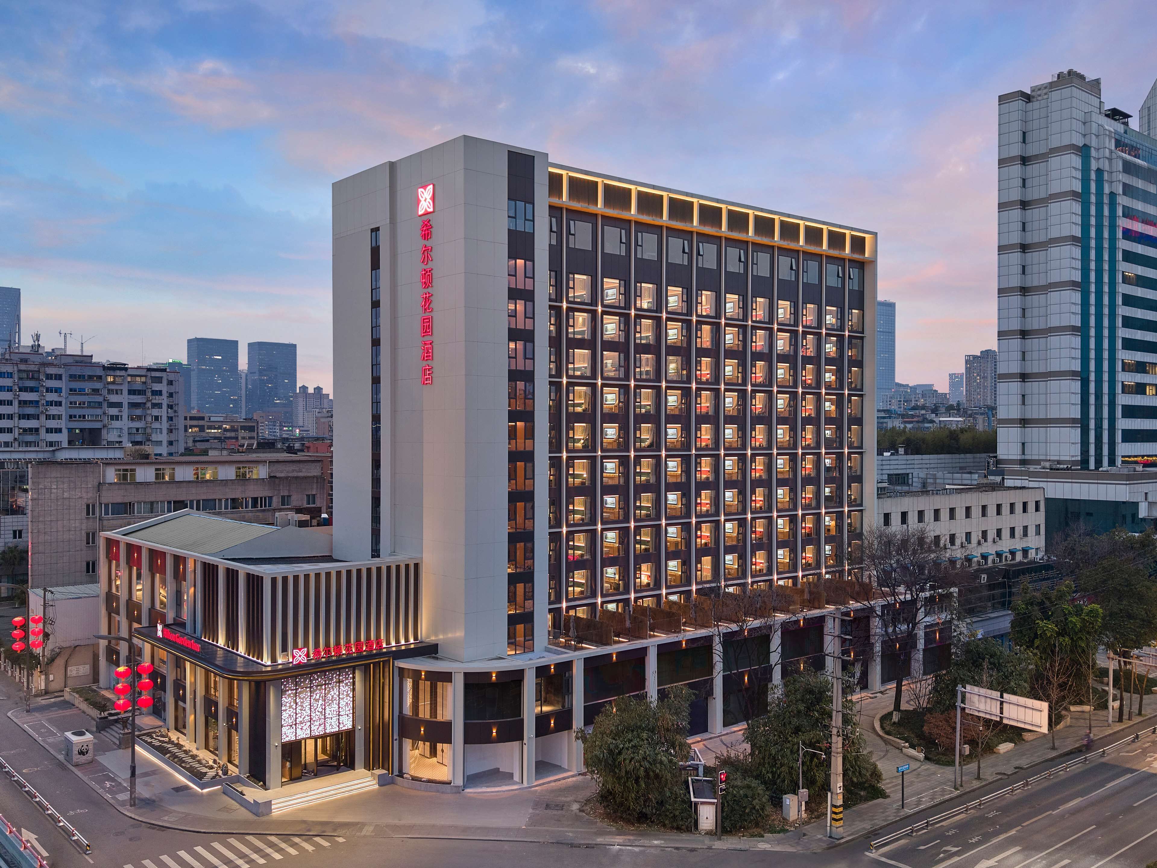 A modern hotel with a prominent vertical sign, a glass facade, and a rooftop terrace.