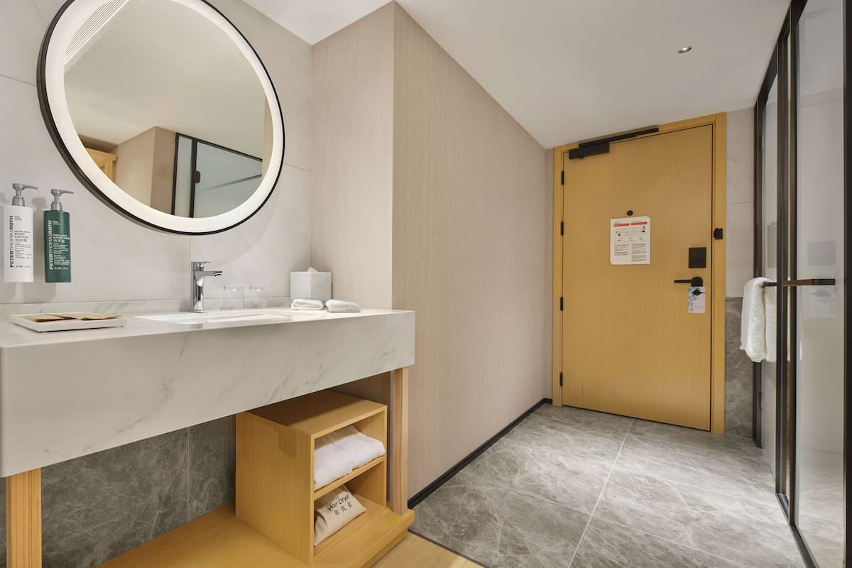 A modern bathroom with a round mirror, a sink, and a wooden shelf.