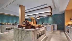 Un vestíbulo de hotel moderno con mostradores de mármol, una pared con azulejos azules y una isla central con opciones de comida y bebida.