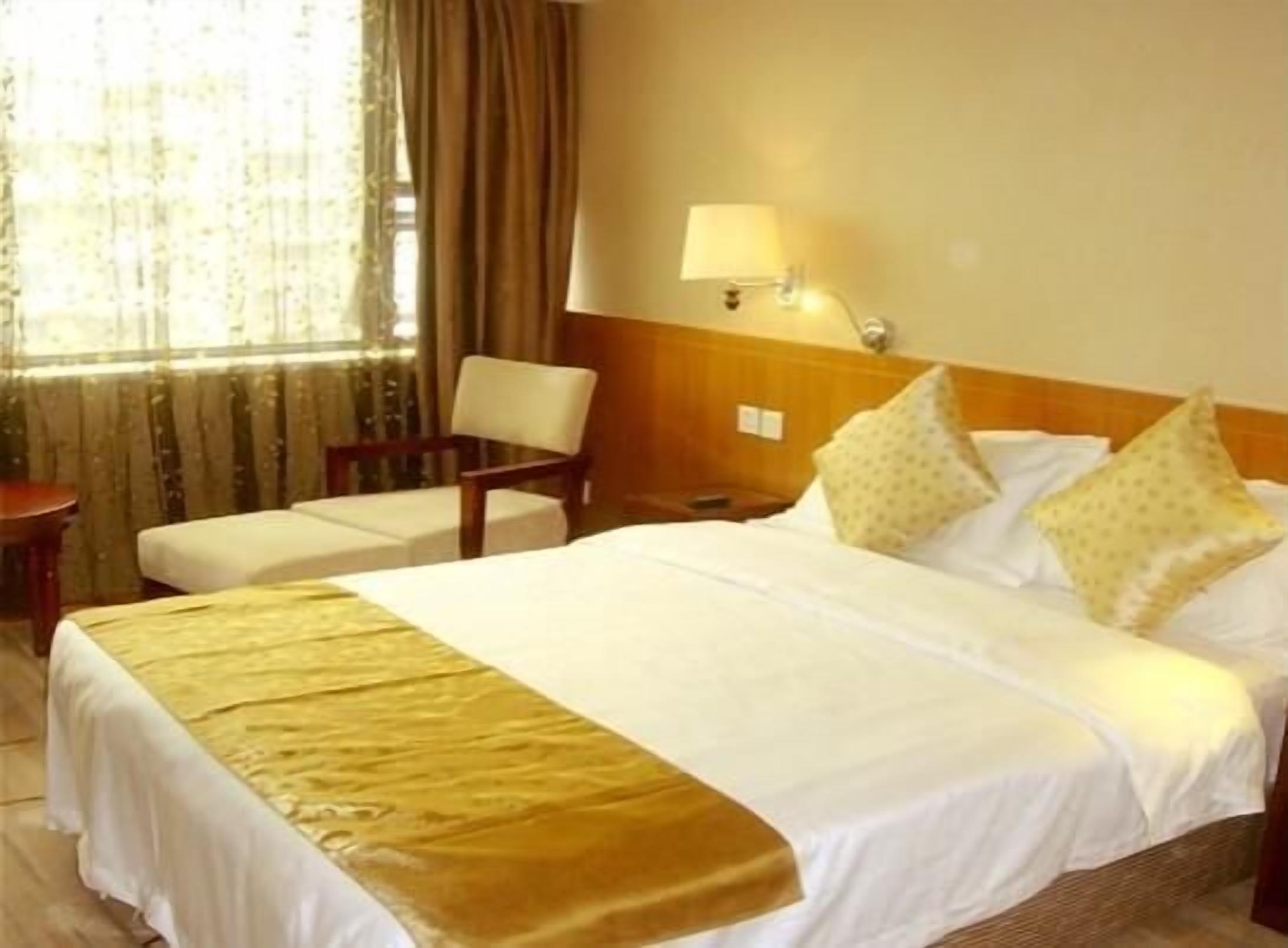 Une chambre d’hôtel avec un lit, une chaise, une lampe et une fenêtre avec des rideaux.