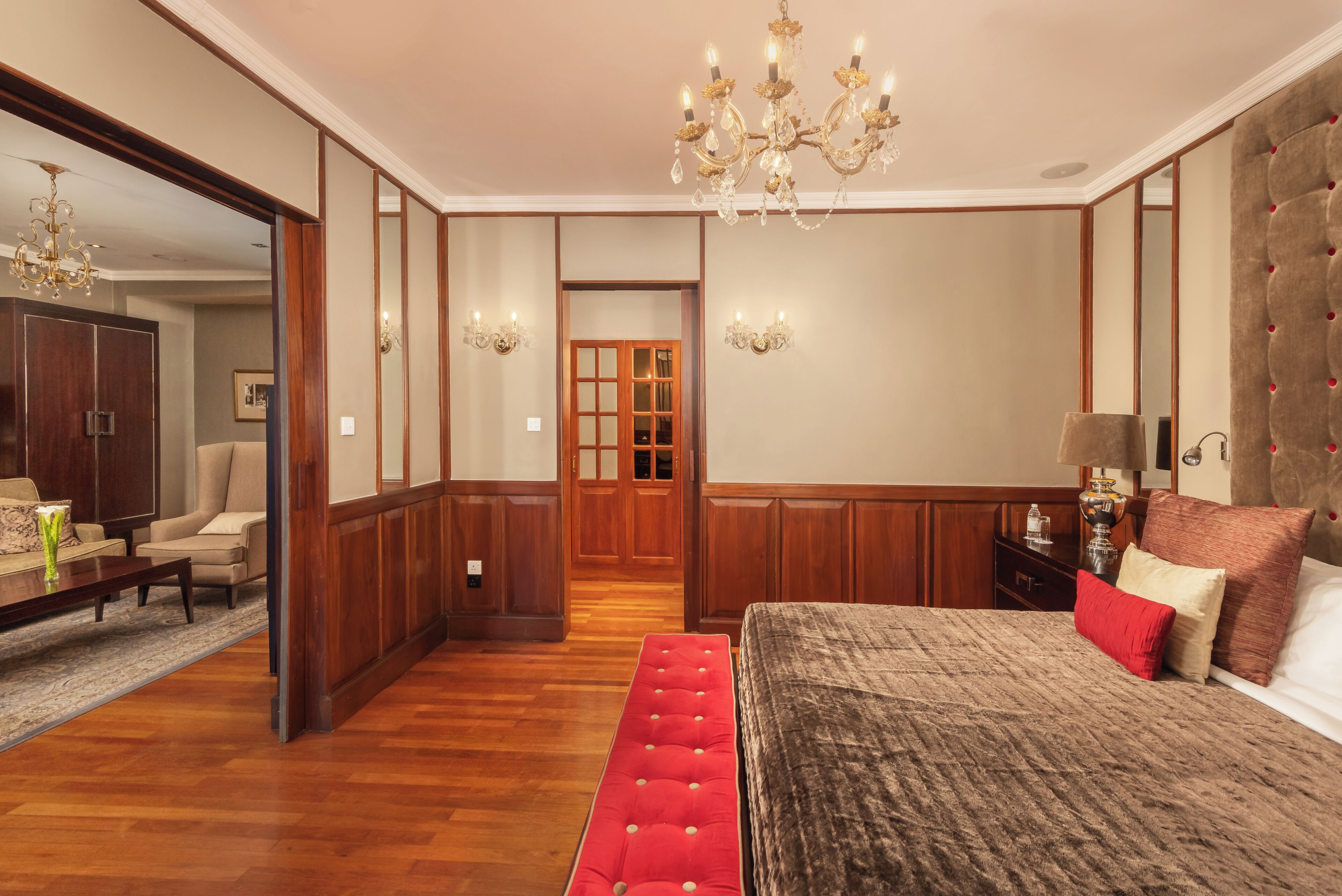 A spacious bedroom with a large bed, a wooden wardrobe, a sitting area with a sofa, and a chandelier.