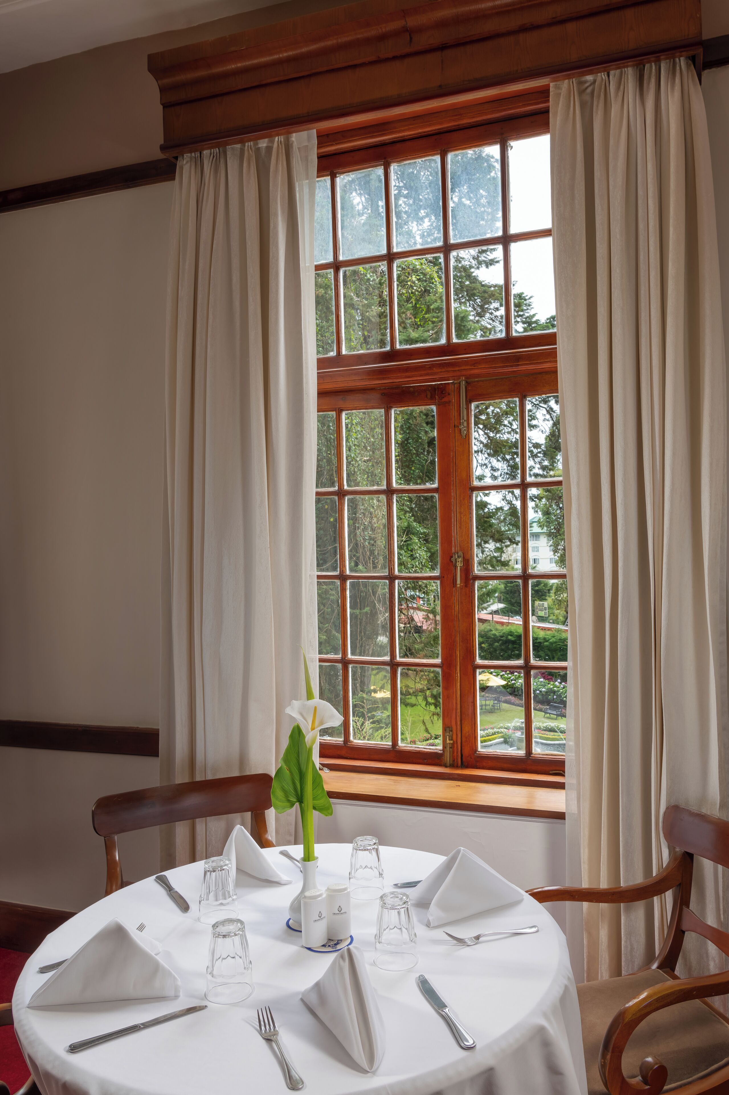 A dining table set for four with a view of a garden through a window.