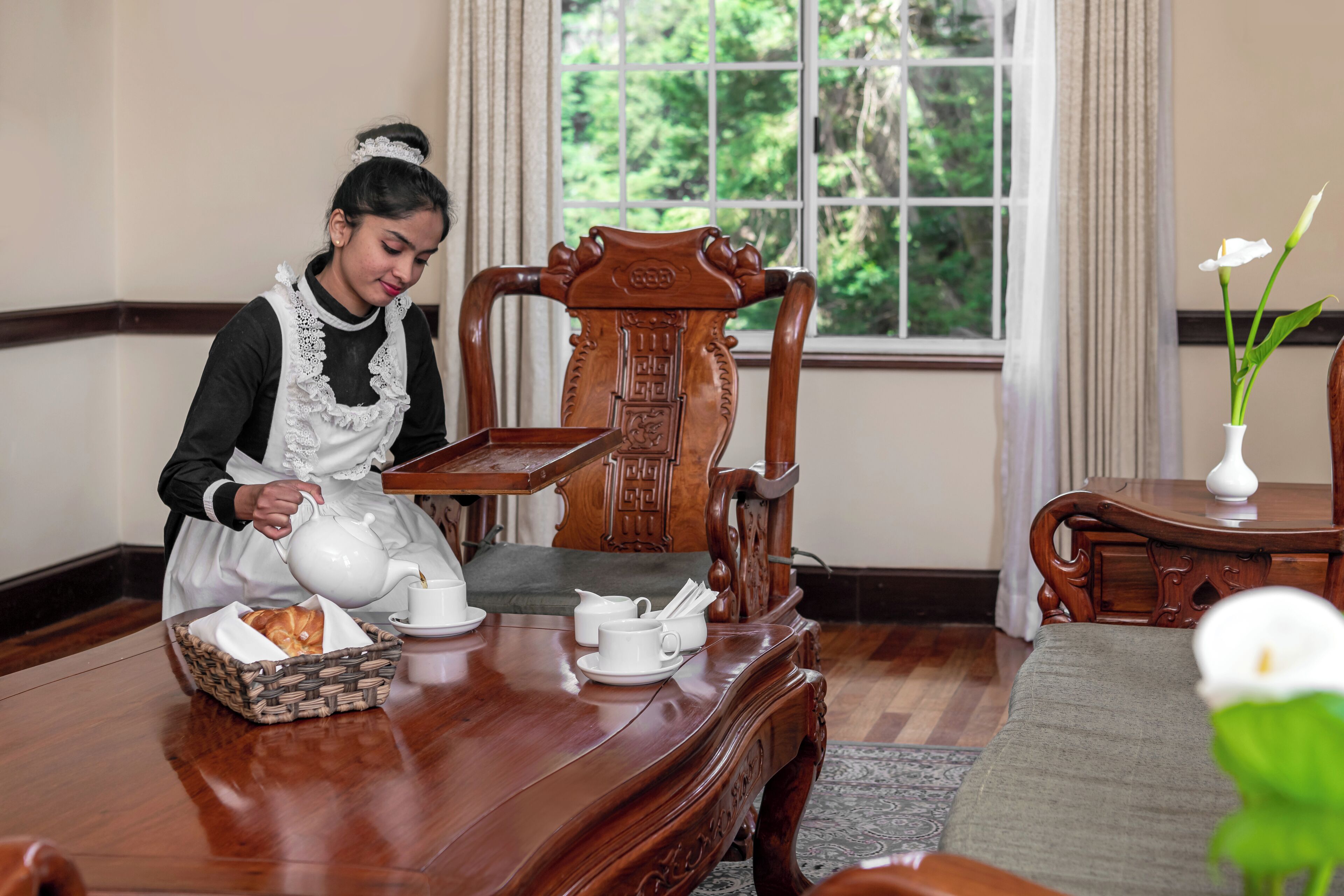 Una persona sirviendo té en una mesa de madera con una bandeja, una cesta de mimbre y tazas de té.