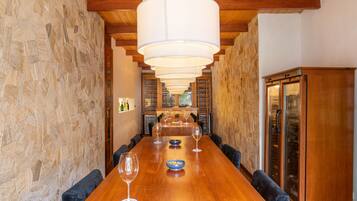 A long wooden table with chairs, a stone wall, and a wine rack in the background.