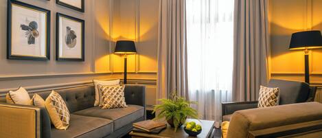 Una sala de estar con un sofá, sillones, una mesa de centro con una planta y un frutero, y obras de arte enmarcadas en la pared.