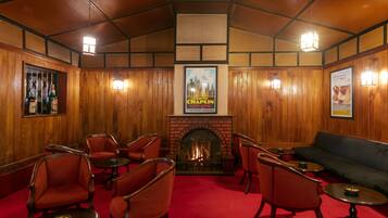 A cozy room with wooden walls, a fireplace, red carpet, and red upholstered chairs.