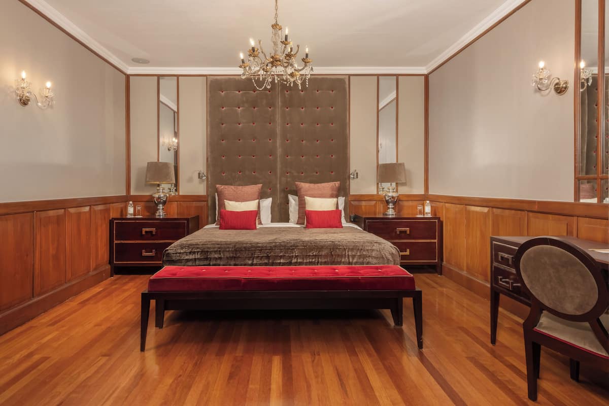 A spacious bedroom with a large bed, a chandelier, wooden paneling, and a mirror.