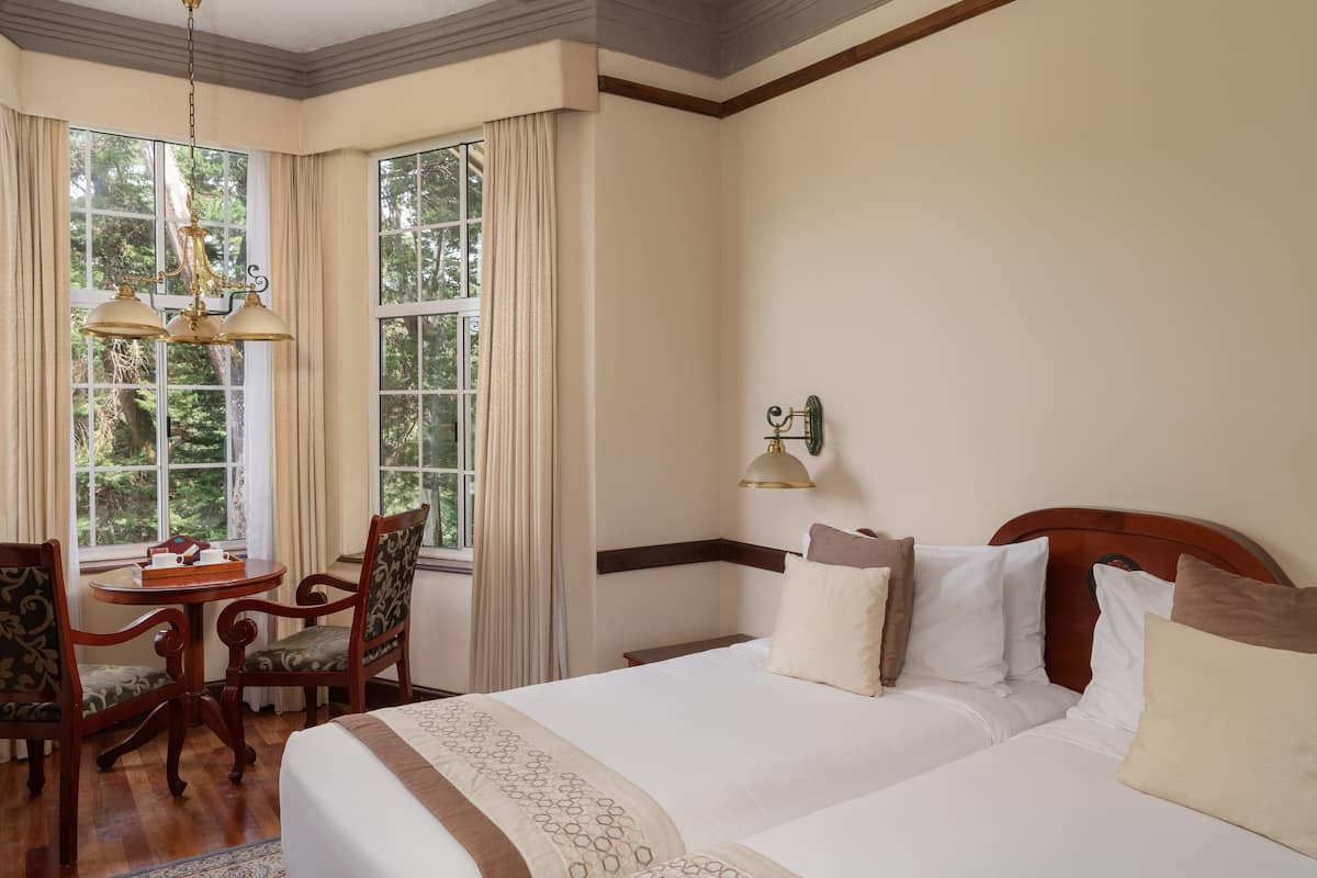 A hotel room with a large bed, a wooden chair, a small table, and a window with curtains.