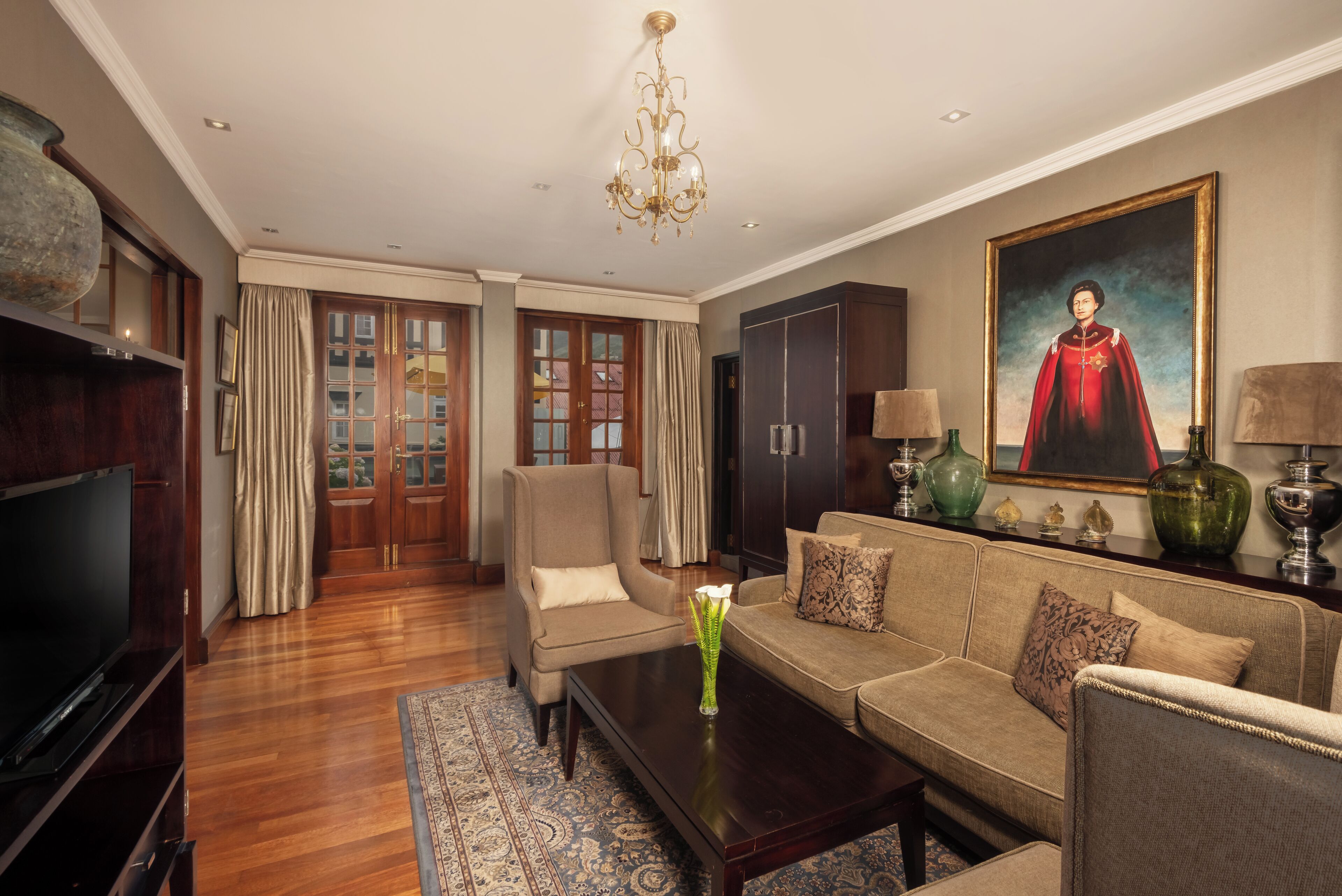 A living room with a sofa, armchair, coffee table, TV, and a painting on the wall.