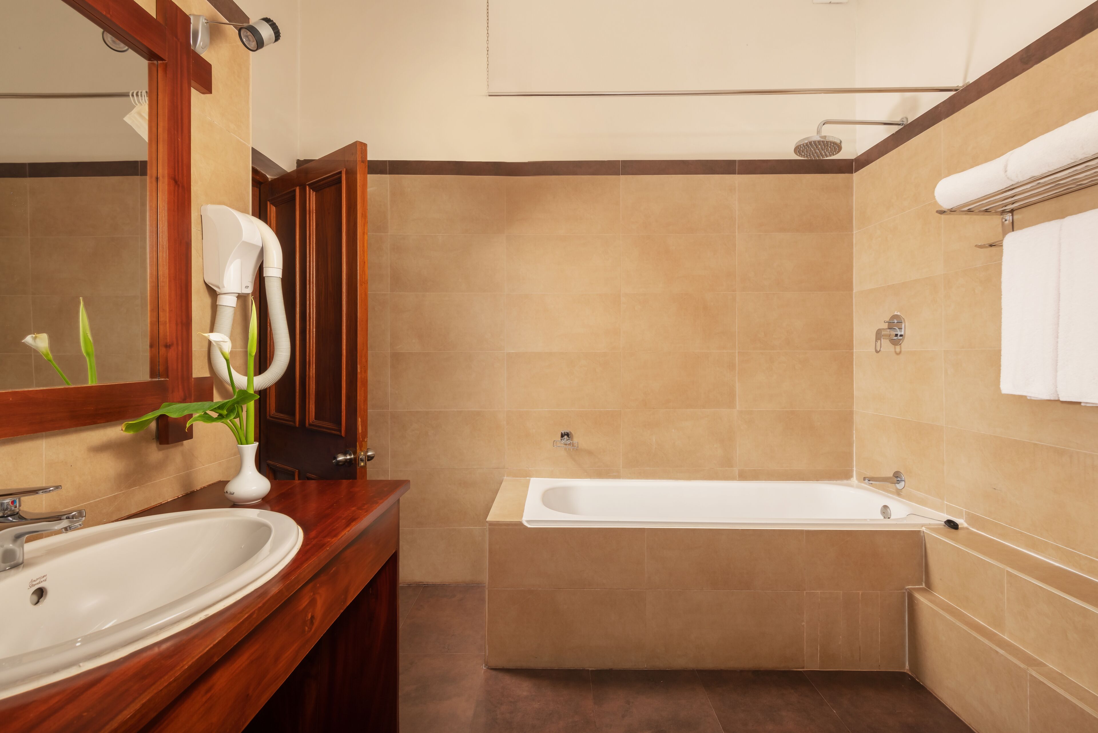 A bathroom with a wooden vanity, a white sink, a large mirror, a shower with a handheld showerhead, and a bathtub.