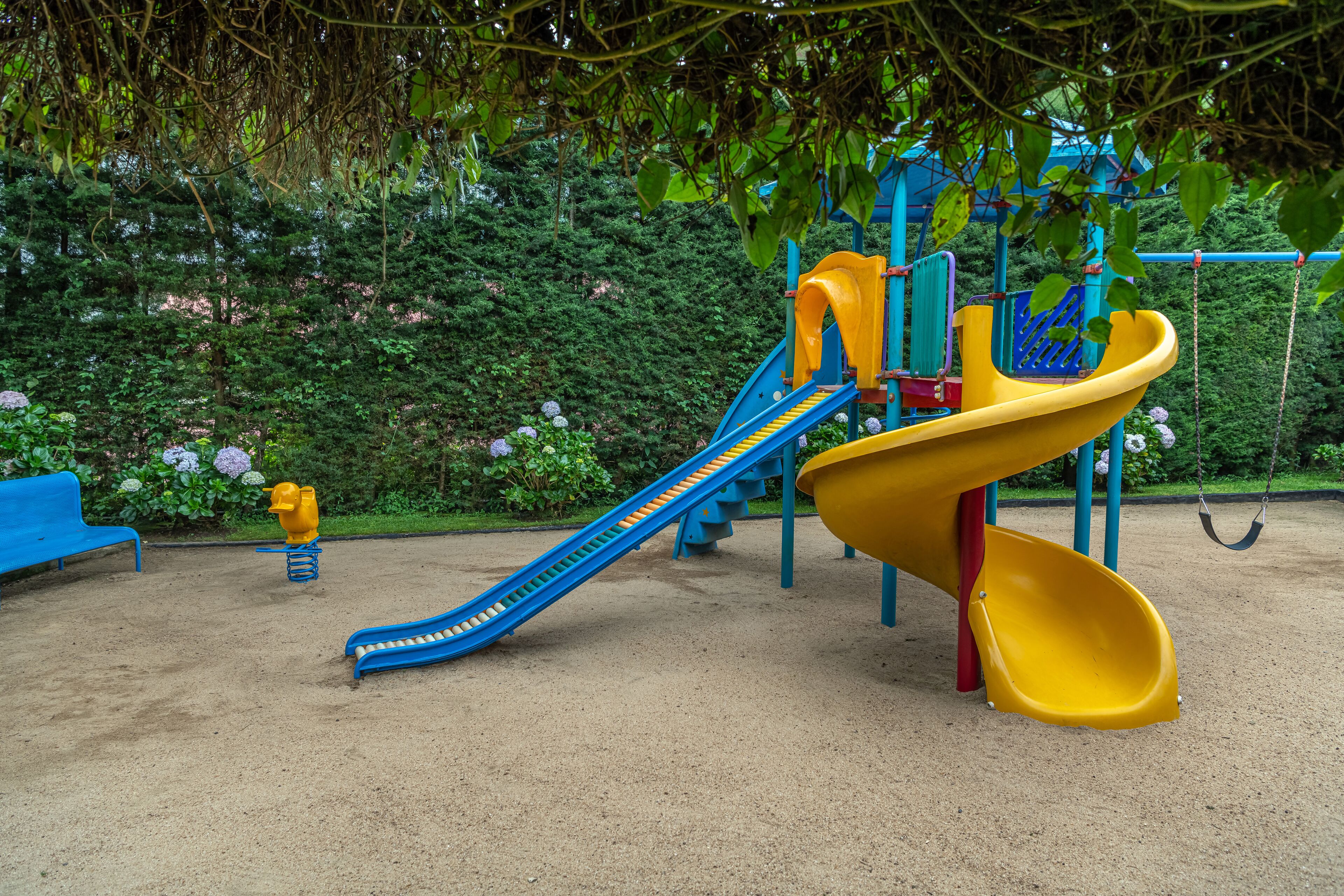 A playground with slides and swings, surrounded by greenery.
