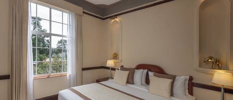 A hotel room with a large bed, two bedside tables, a window with curtains, and a mirror on the wall.