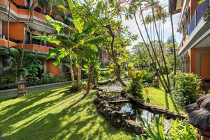 A courtyard with a small pond, lush greenery, and a traditional building with balconies.
