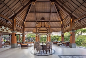 A covered outdoor dining area with a central table and chairs, surrounded by benches and sofas.