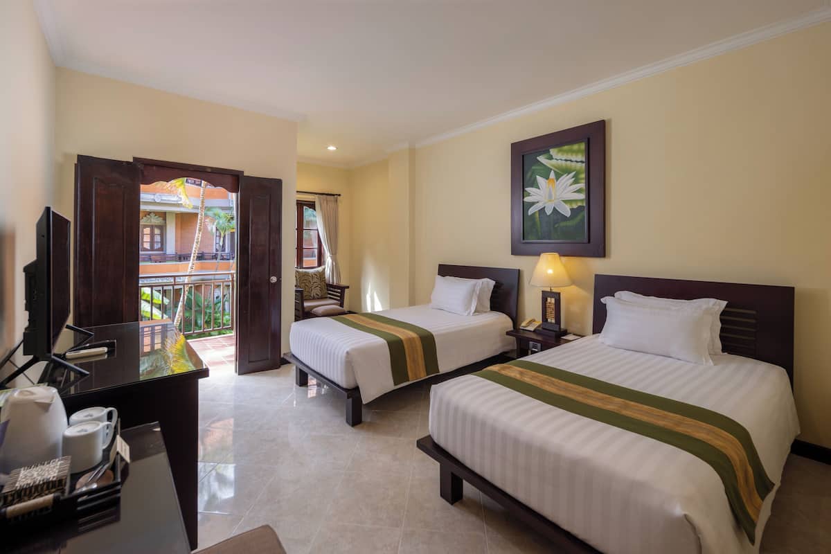 A hotel room with two beds, a desk with a telephone, and a balcony with a view of a building.