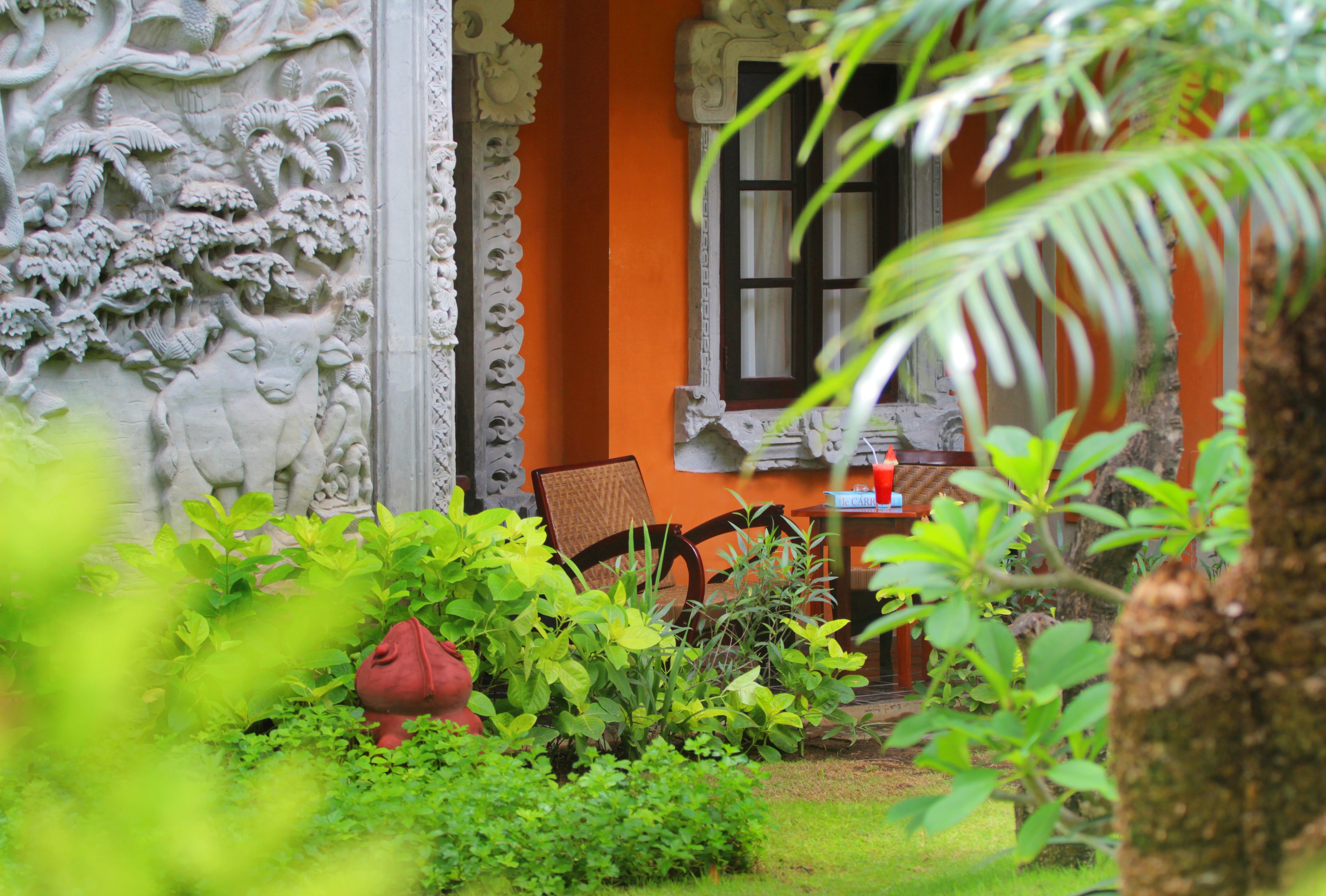 Un jardín con una silla, una mesa, una estatua y un edificio naranja con una ventana.