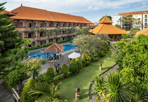 A hotel with a swimming pool surrounded by lush greenery and a well-maintained lawn.