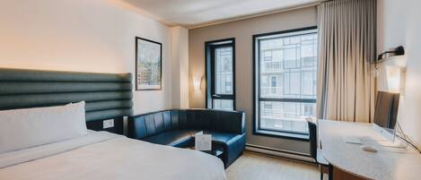 Et hotelværelse med seng, skrivebord, stol, sofa og store vinduer.