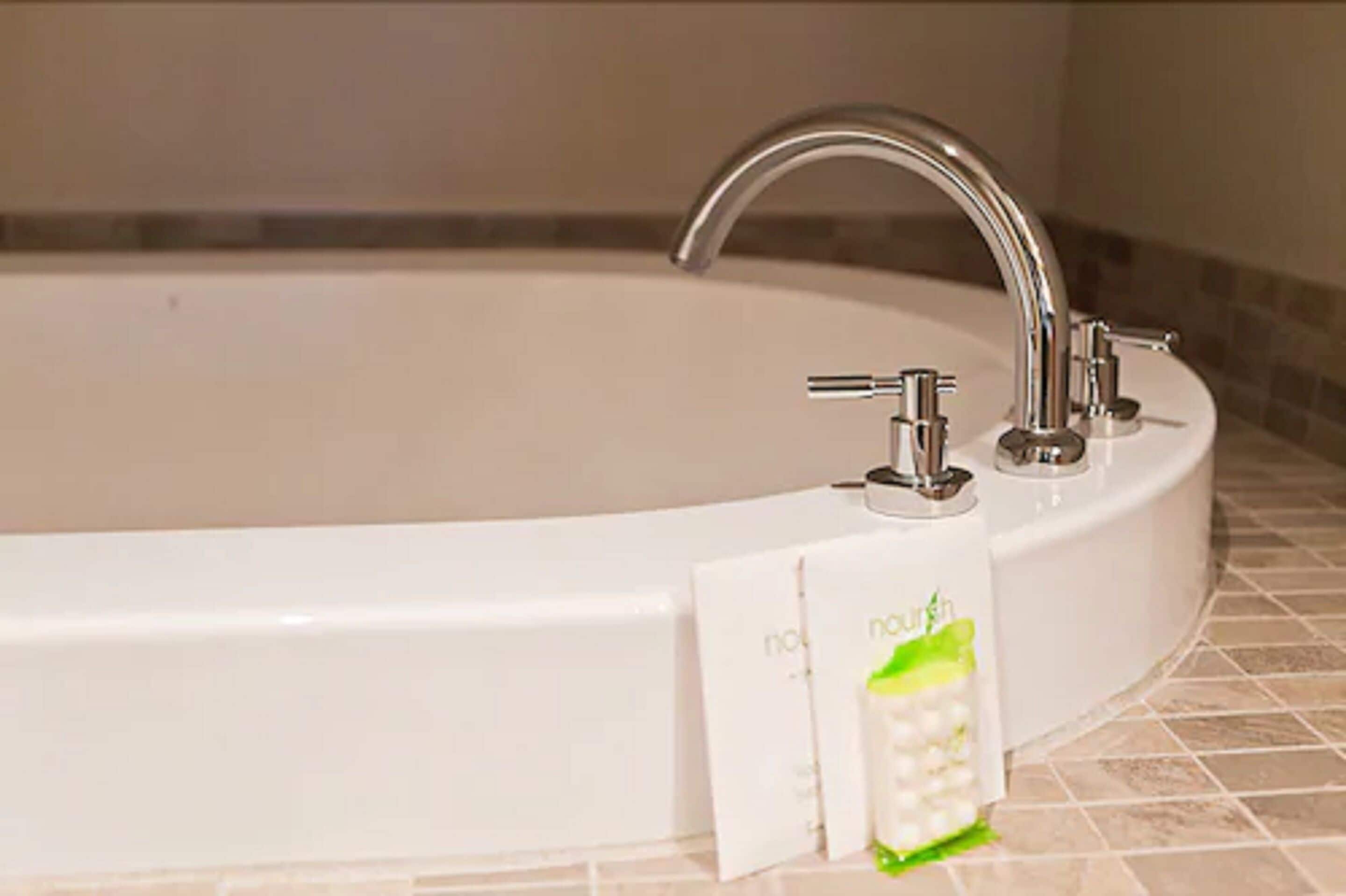 Una bañera blanca con un grifo moderno y dos dosificadores de jabón a los lados.