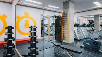 Un gimnasio con equipo de ejercicio, espejos y una banca roja.