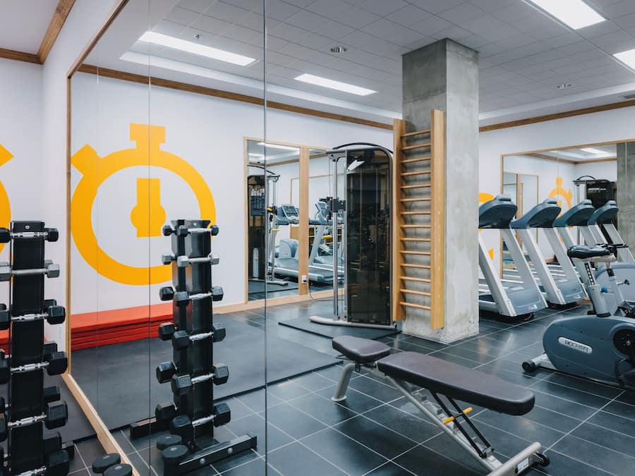 Un gimnasio con equipo de ejercicio, espejos y una banca roja.